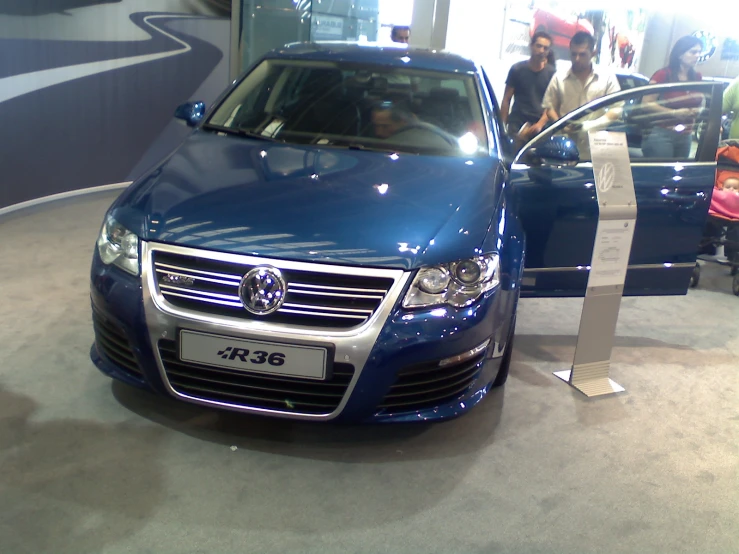 a blue car parked in a showroom filled with people