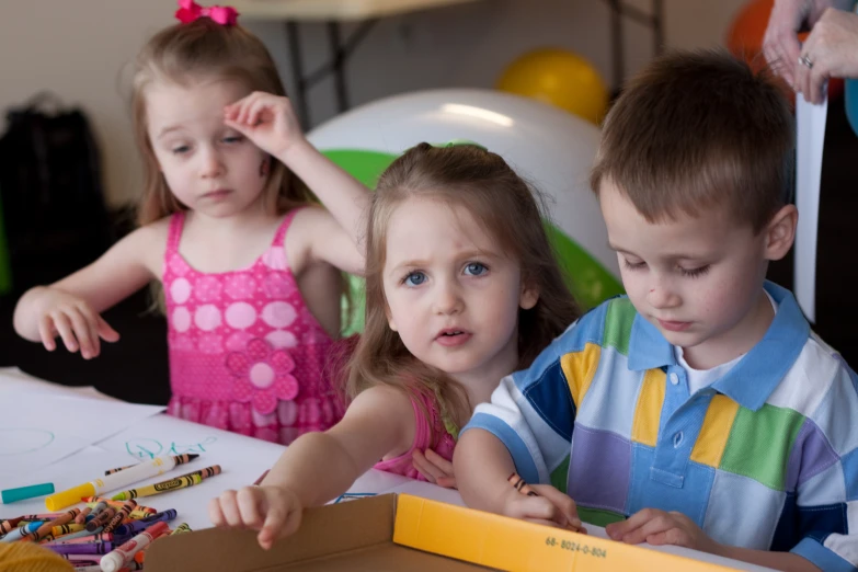 two children at table with toys including pencils