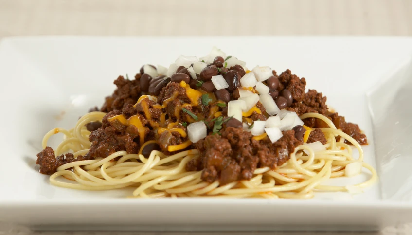 spaghetti with chili and cheese is on a white square plate