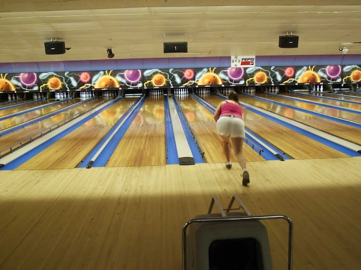 a woman walking through bowling alley in pink shirt