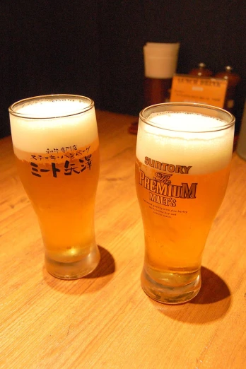 two tall glasses with beer sitting on top of a table