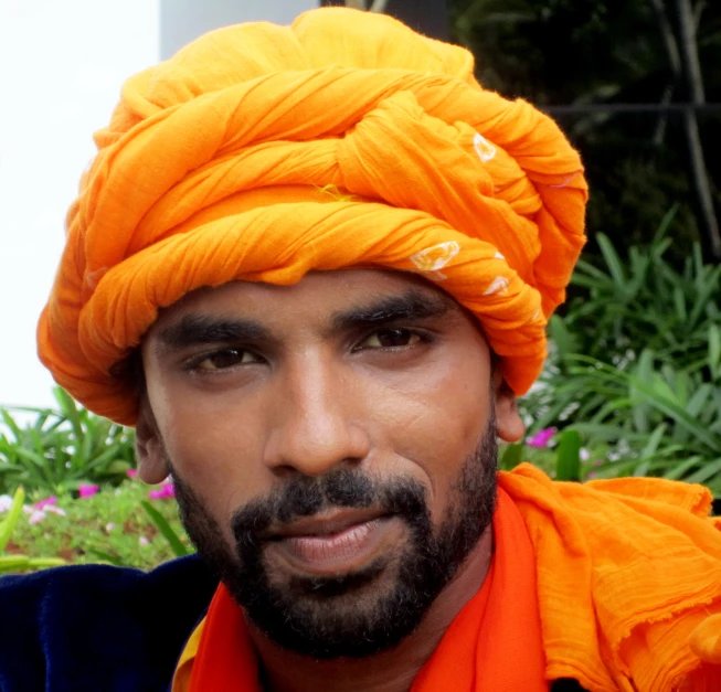 a bearded man wearing an orange turban smiles for the camera