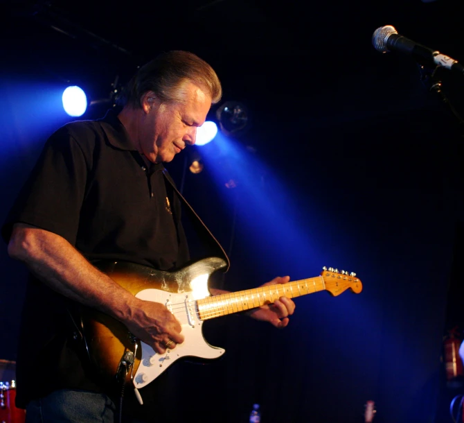 a man holding his guitar on stage in front of microphone