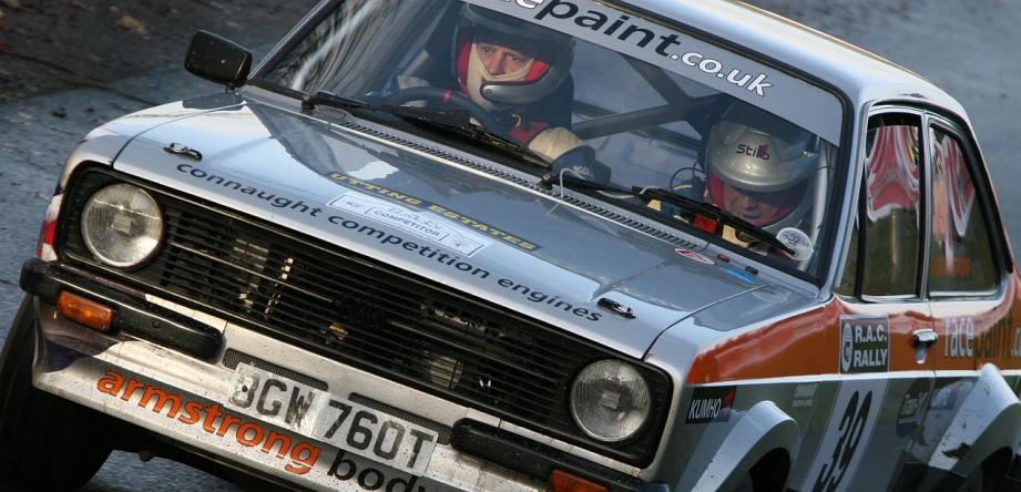 an older man driving a vintage rally car on a road