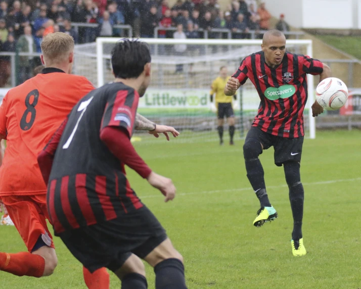 a soccer player with a ball in his hands while two players are on the field and a crowd watches