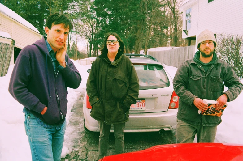 three people standing in the snow near cars