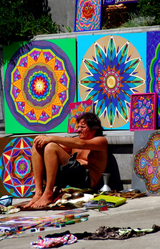 a man sitting on the ground next to some very colorful wall hangings