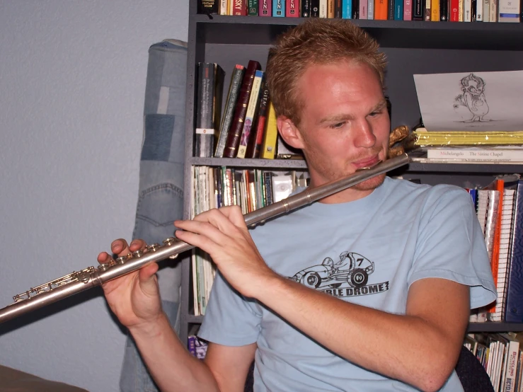 a man plays the flute in front of a bookshelf