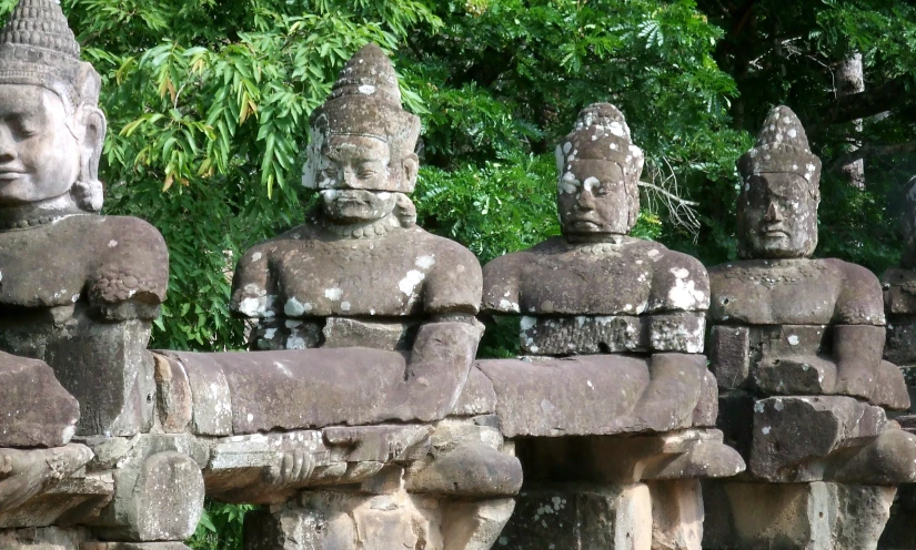 seven statues sit on concrete pillars in front of trees