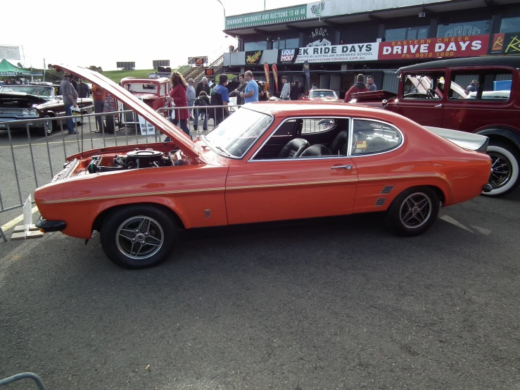 an orange car is sitting outside near a crowd