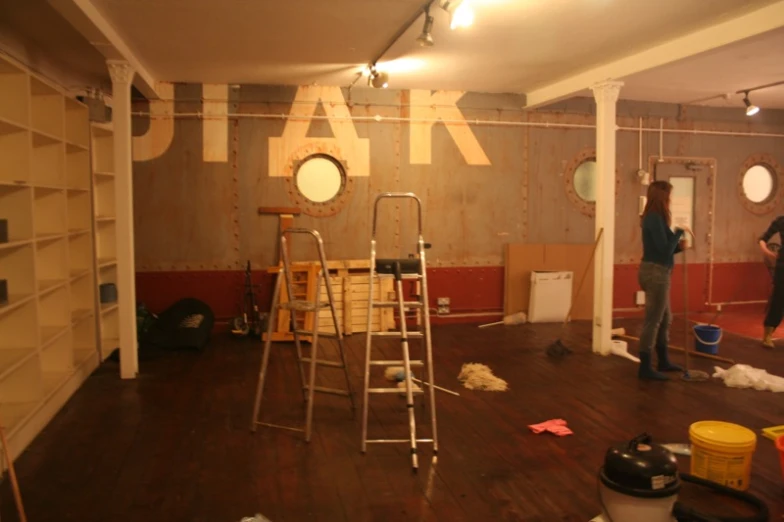 two people stand next to a ladder in a room with an unfinished floor