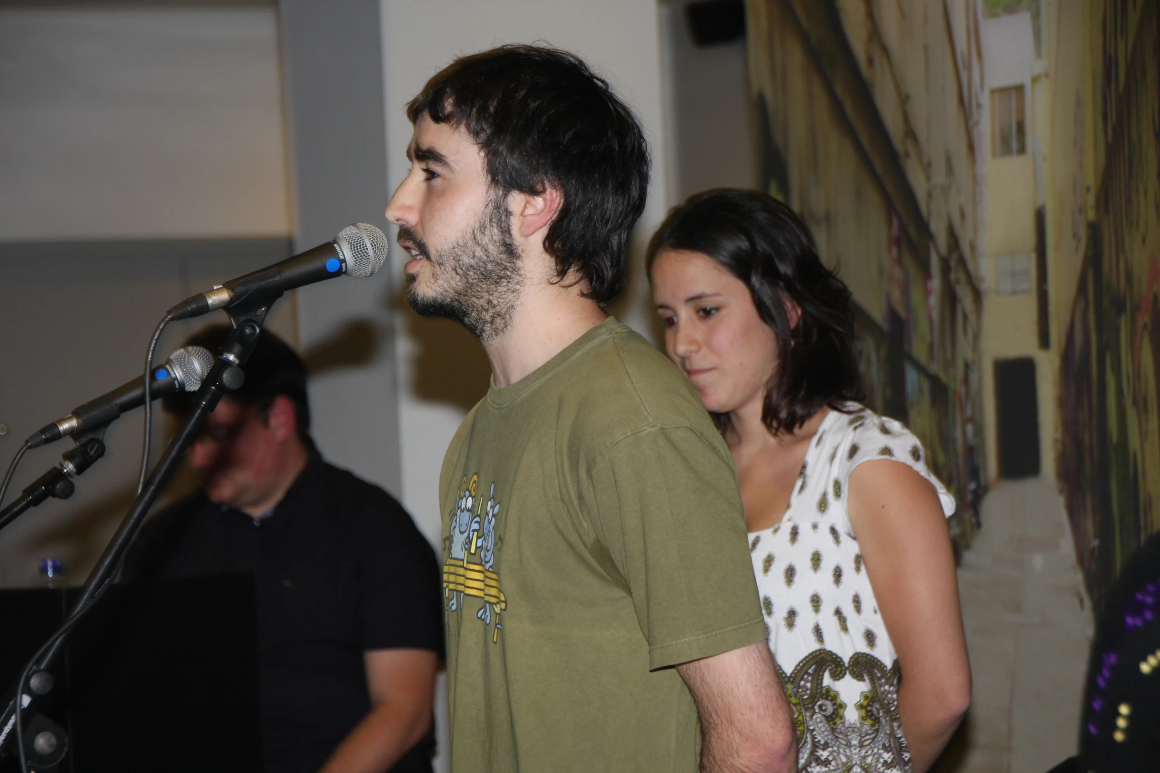 a man singing in front of microphone in room with a woman