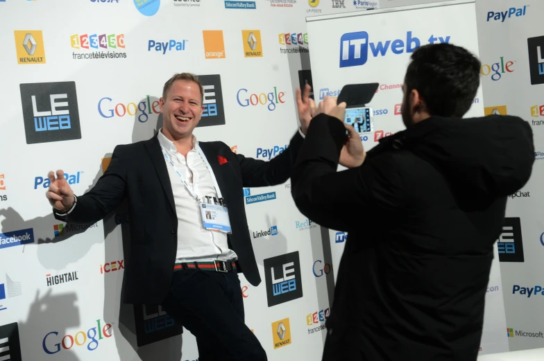 two men pose for pictures in front of a backdrop