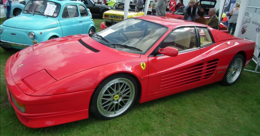 a red car sitting on top of green grass next to other cars