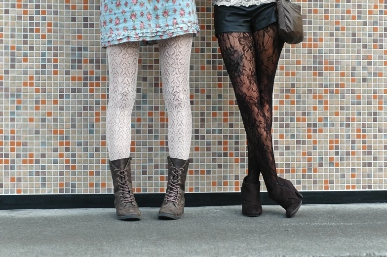 two women are standing on a sidewalk with their legs crossed