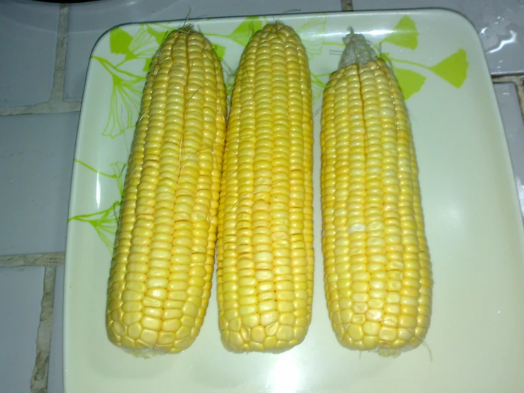 three ear of corn on a plate with other vegetables