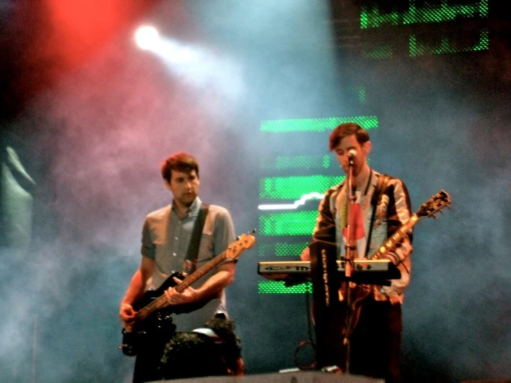 two guys with guitars on stage performing in front of light beams