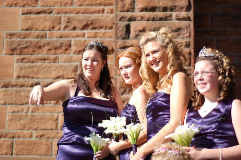 some girls are standing in front of a brick wall and wearing purple dresses