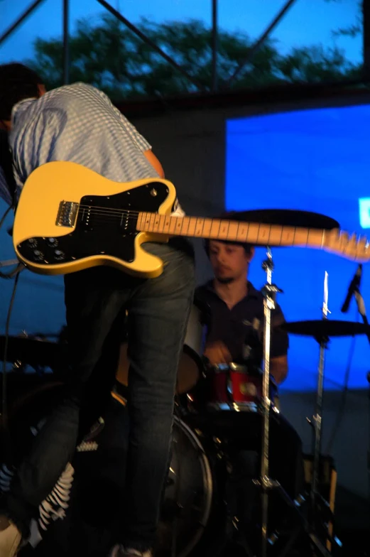 man playing on yellow electric guitar and another male with musical equipment