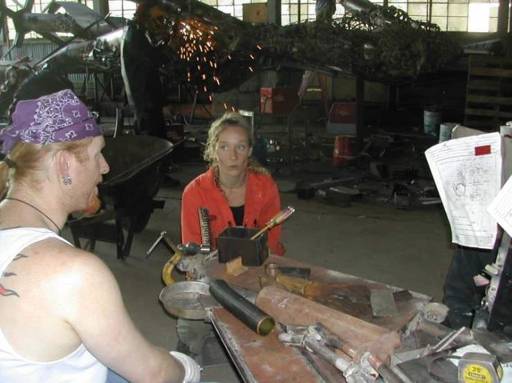 a woman who is sitting down at a table and someone that is holding a drill