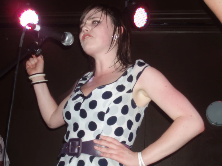 a woman is singing into a microphone while wearing a polka dot dress