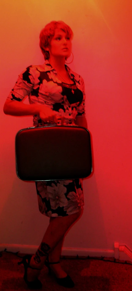 a woman with black and pink shoes and a flowery dress, holding a suitcase