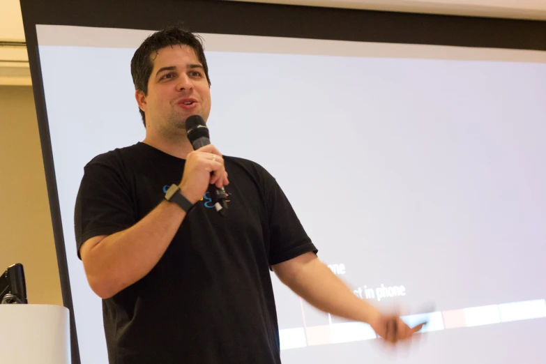 a man holding a microphone up while standing in front of a projection screen