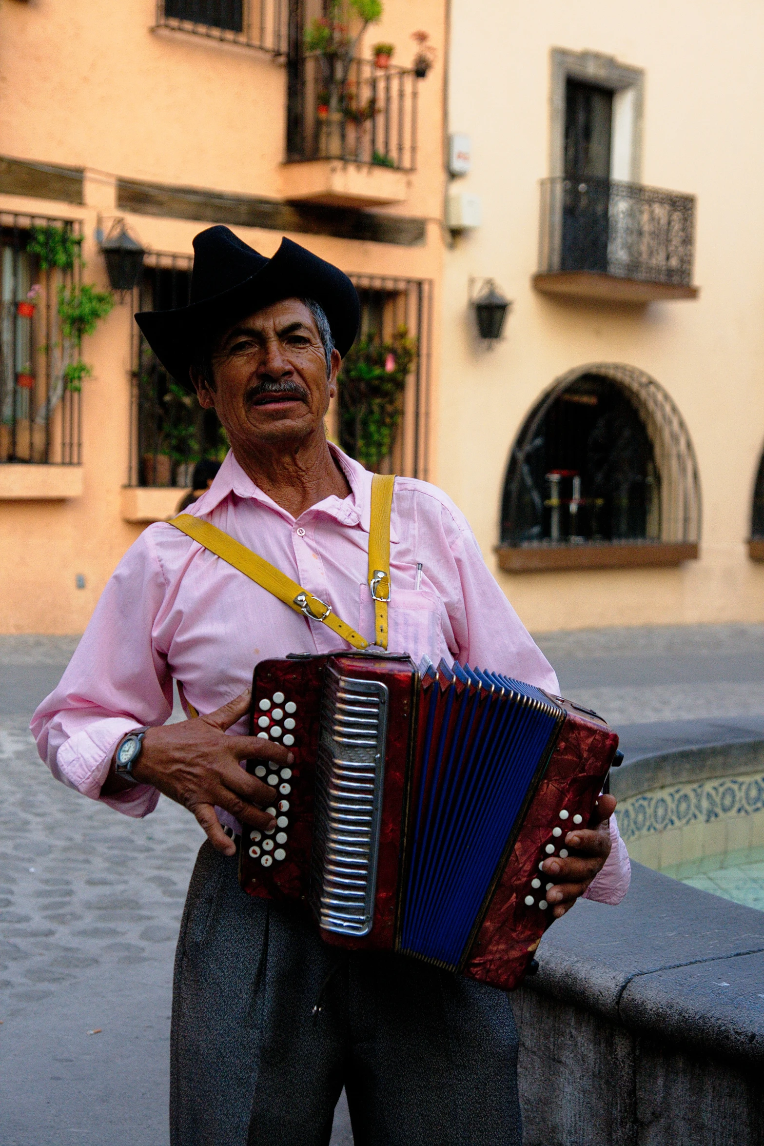 a man in a pink shirt and hat holding a red accordion