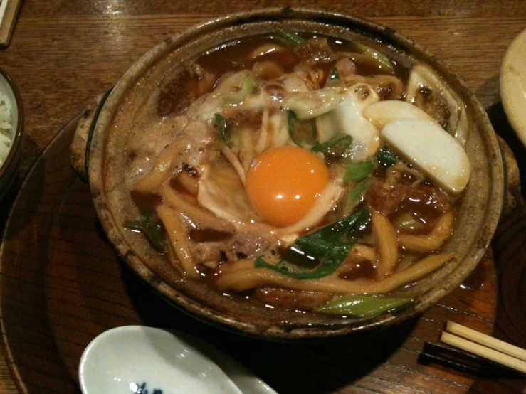 bowl of noodles with egg on top sits on wooden table