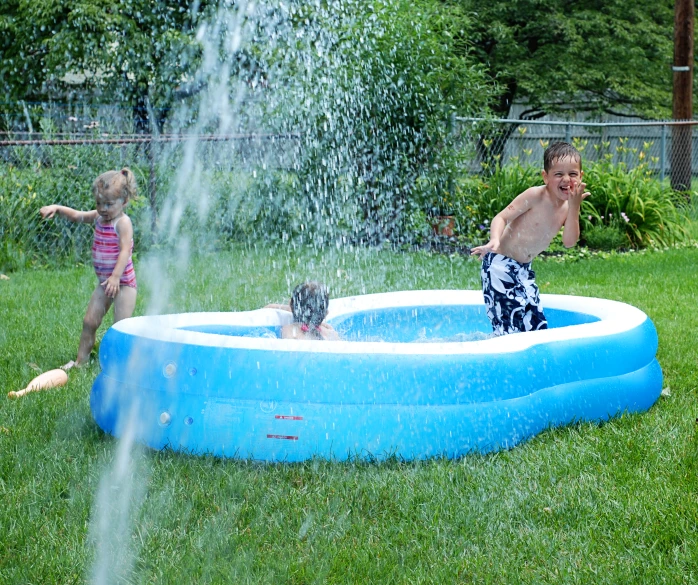 a boy and a girl playing with a d's swimming pool in the backyard