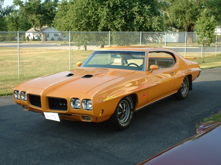 an orange car parked next to a car in a field