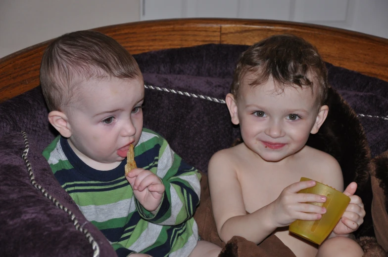 two babies sitting on the couch playing with toothbrushes