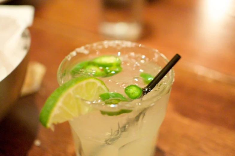 a glass with ice and lime on top next to a brown table