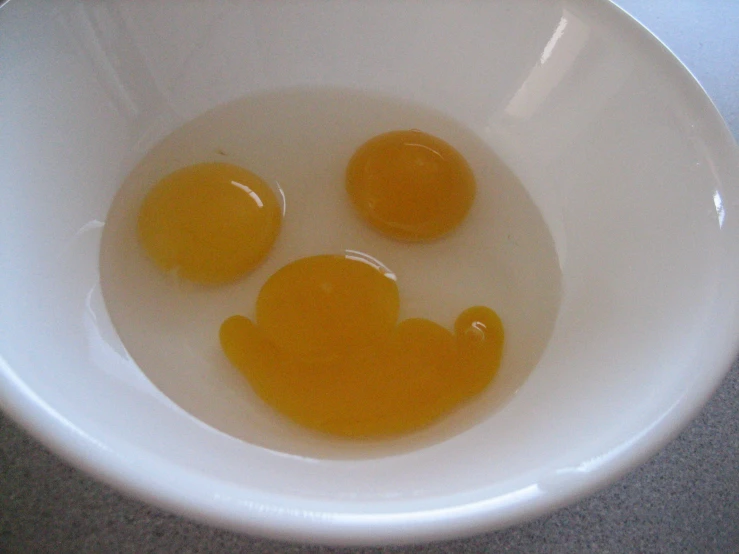 the eggs are in the white bowl and have the shape of smiley face drawn on them