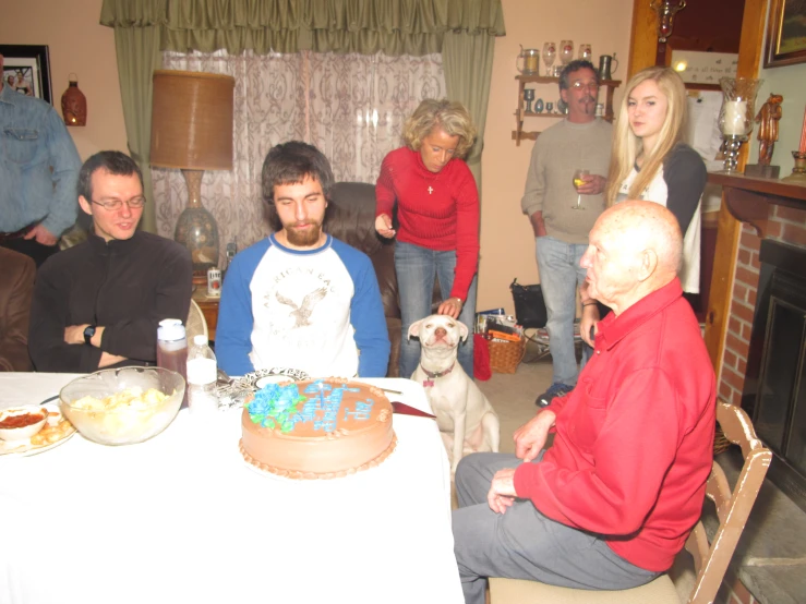 a group of people are gathered around a table with a cake