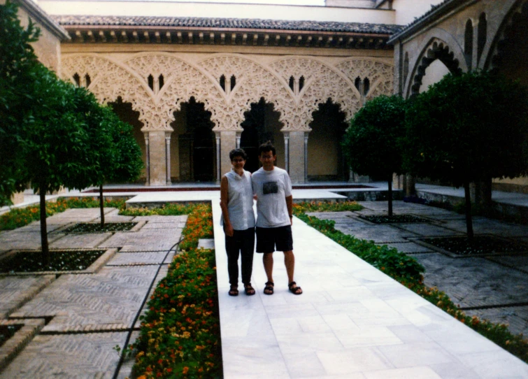 two men standing in a courtyard between some trees