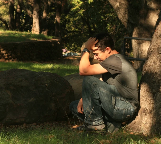 a man is sitting on a rock next to a tree and reading