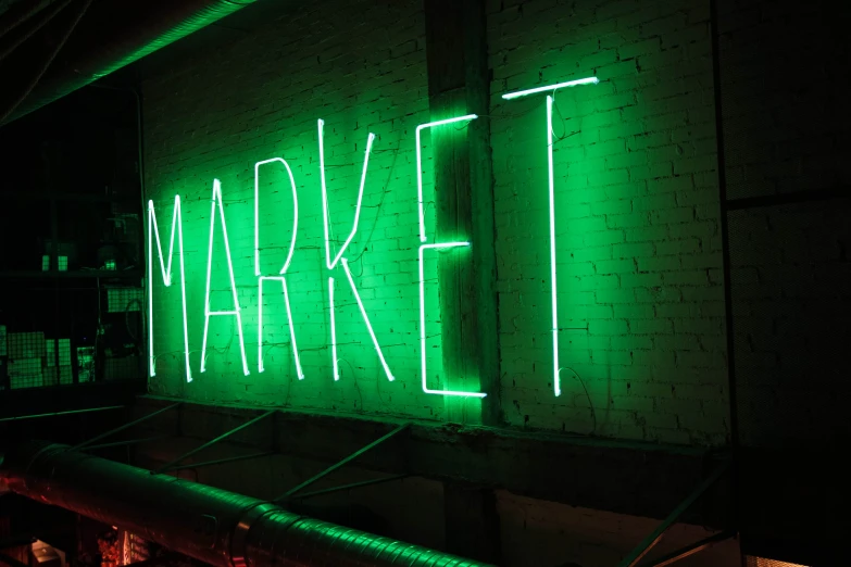 green neon sign that reads market next to a white brick wall