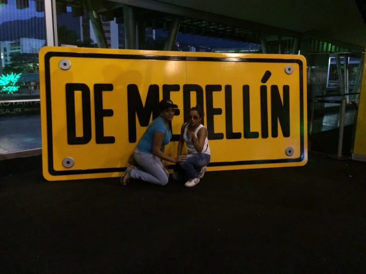 two people sit against a yellow sign with german words