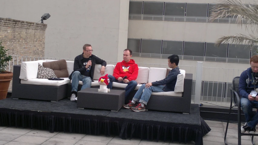 three men sit on couches while each holds a bottle