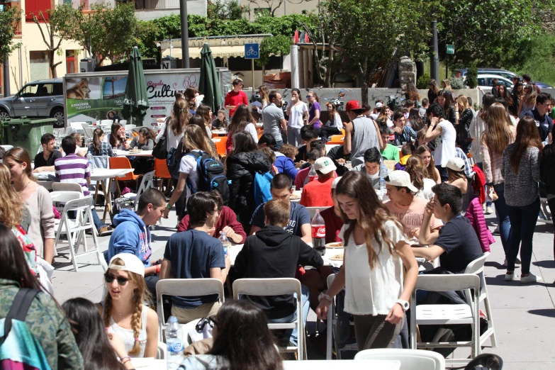 a large group of people sit on the sidewalk eating, talking and drinking