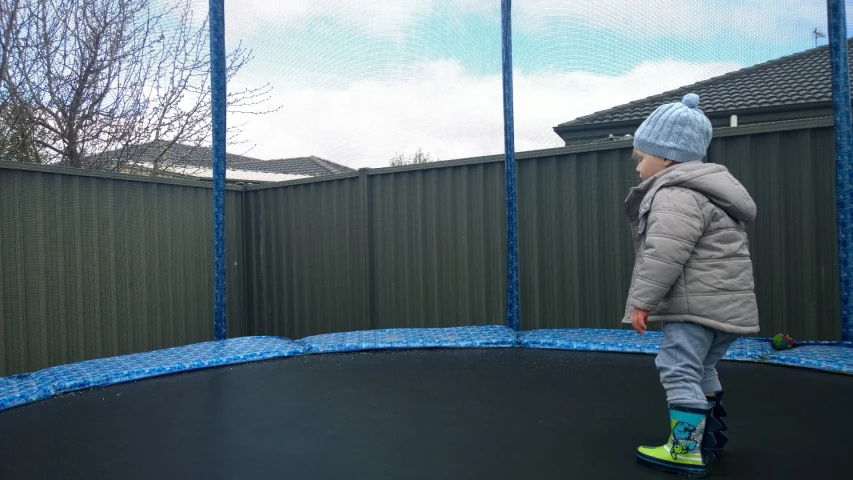 small child on a trampoline, facing an open fence