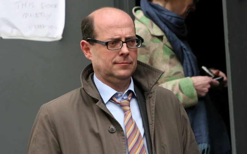 an older man with a coat and tie walking into a house