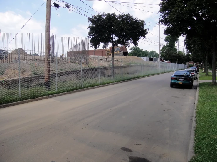 two cars are driving down the street past a fence