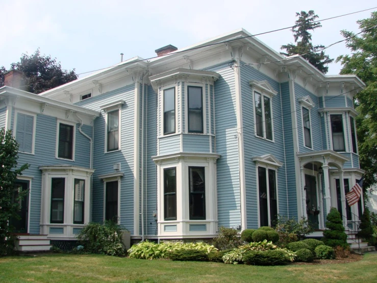 blue two story house with grass and shrubs in front