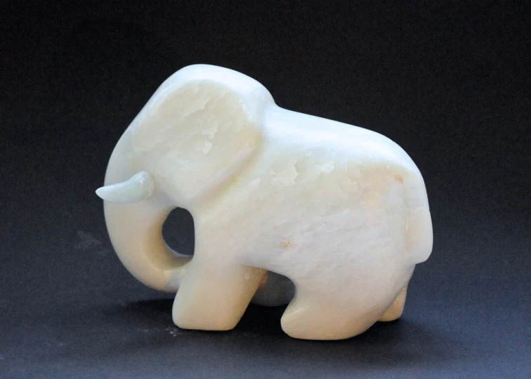 a white elephant made of marble sits on black surface