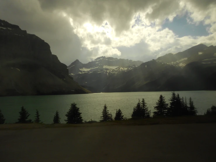 there are clouds above a large lake that has pine trees in it