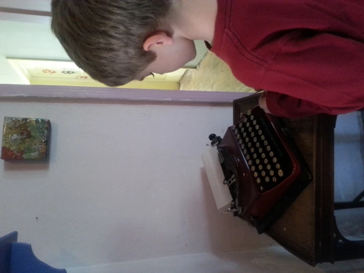 a boy sits at a desk and looks down at a typewriter