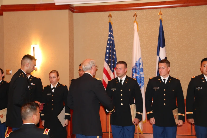 men in uniform at a ceremony with two men shaking hands