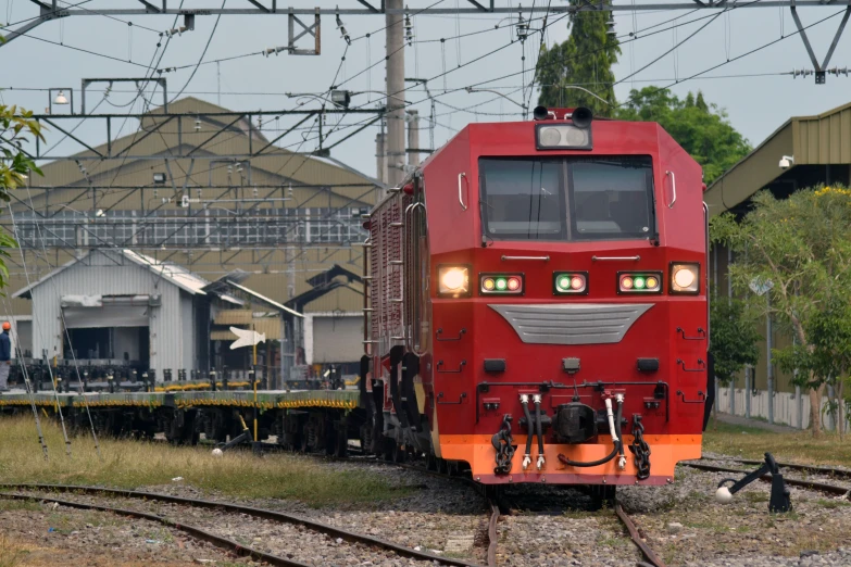 a red train traveling past a row of industrial buildings